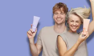Glad man och kvinna ler och håller upp hårinpackningar. Hon har protein repair, han har blonde.