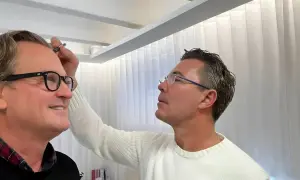 Man med glasögon får styling av sitt permanenta hår.