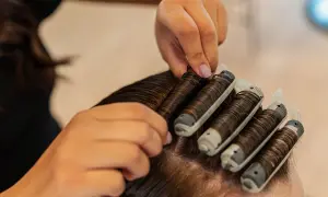 Hårstylist sätter i permanentrullar i mörkt hår. En del av processen för att se hur lång tid det tar att permanenta håret.