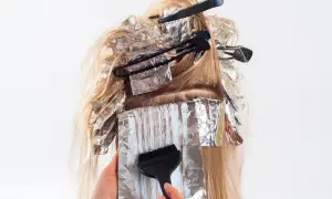 Hårstylist applicerar färg med pensel på slingor i blont hår, insvepta i folie. En blivande mamma som vill fräscha upp sitt hår.