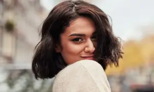 A woman with dark, wavy bob haircut and a nose ring smiles over her shoulder.