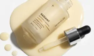 En flaska med "RADIANT 15% VITAMIN C BOOSTER" serum ligger på en gulaktig vätska. Pipetten har en droppe pha syra redo att appliceras.