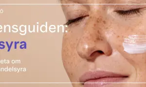 En närbild på en kvinna med fräknar som applicerar kräm. Texten lyder "Ingrediensguiden: Mandelsyra".