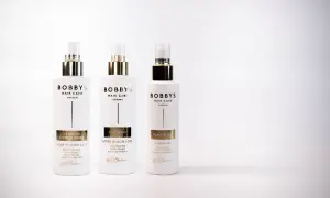 Tre flaskor Bobby's Hair Care i vitt med gulddetaljer. En leave-in conditioner för värmeskydd, en saltspray för beach look och en scalp elixir med rosmarindoft.