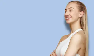 En kvinna med blont hår i en elegant wet look-stil ler mot sidan. Hennes hår är slätt och glansigt, och hon bär en vit topp.