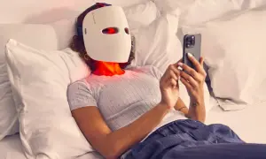 Person med led mask ansikte ligger i sängen och scrollar på mobilen.
