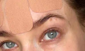 Närbild på ögon och panna med hudfärgad face taping. Ögonen är gröna och har långa fransar.
