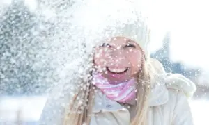 Glad tjej i snöfall, med mössa och halsduk. Solskydd på vintern är viktigt, även när det snöar.
