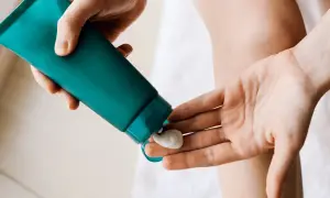 En hand klämmer ut en klick body lotion i ansiktet för återfuktning.