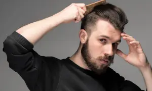 Man med skägg och mustasch stylar sitt korta hår med en kam. Frisyr med skin fade.
