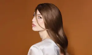 En kvinna med glansigt brunt hår och en subtil nyansering hemma, blickar bort med en mjuk makeup.