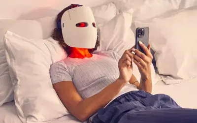 Person med led mask ansikte ligger i sängen och scrollar på mobilen.