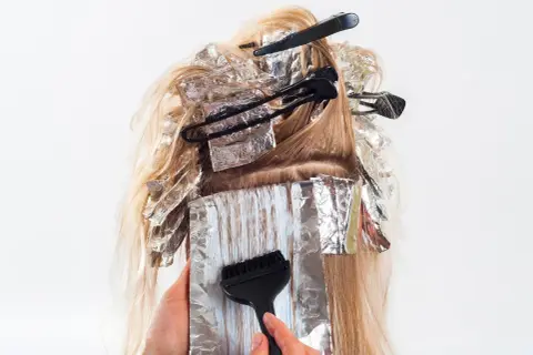 Hårstylist applicerar färg med pensel på slingor i blont hår, insvepta i folie. En blivande mamma som vill fräscha upp sitt hår.