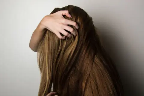 En hand drar genom tjockt, brunt hår. Kanske är det dags för lite biotin för håret för att hålla det friskt och starkt.