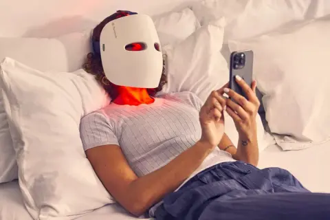 Person med led mask ansikte ligger i sängen och scrollar på mobilen.
