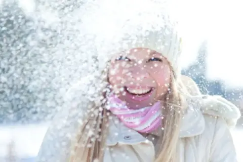 Glad tjej i snöfall, med mössa och halsduk. Solskydd på vintern är viktigt, även när det snöar.