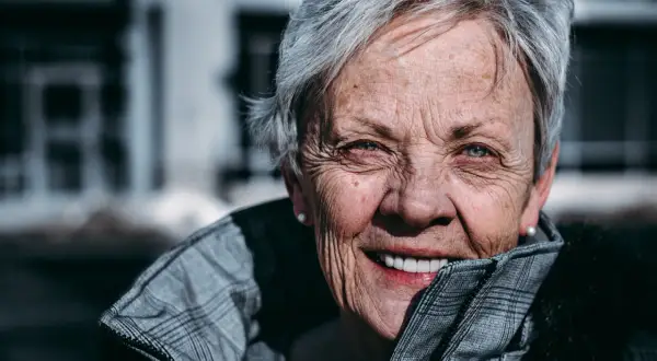 En kvinna med grått hår och korta frisyrer, runt 60 år, ler varmt. Hon bär en rutig jacka.