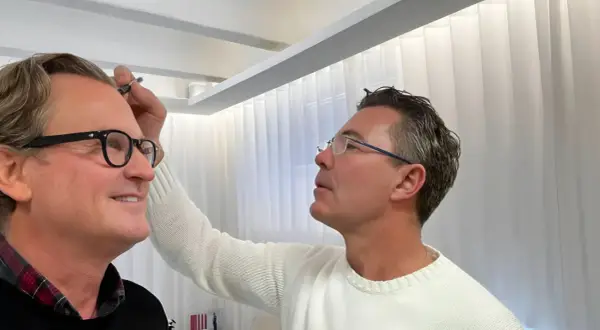 Man med glasögon får styling av sitt permanenta hår.
