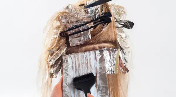 Hårstylist applicerar färg med pensel på slingor i blont hår, insvepta i folie. En blivande mamma som vill fräscha upp sitt hår.