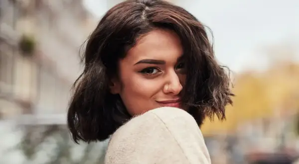 A woman with dark, wavy bob haircut and a nose ring smiles over her shoulder.