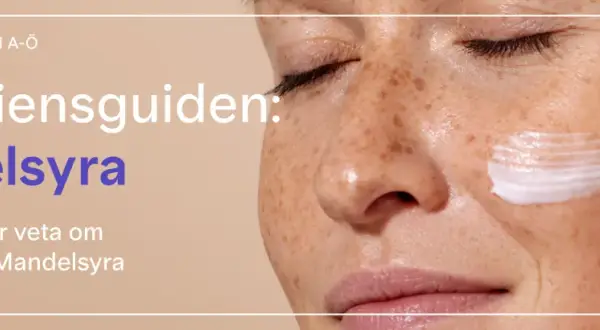 En närbild på en kvinna med fräknar som applicerar kräm. Texten lyder "Ingrediensguiden: Mandelsyra".