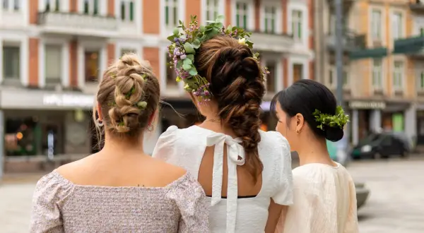Tre kvinnor med vackra frisyrer, en med blomsterkrans, en med flätor och en med knut, visar upp sina hår.