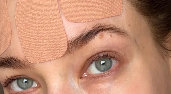 Närbild på ögon och panna med hudfärgad face taping. Ögonen är gröna och har långa fransar.