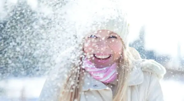 Glad tjej i snöfall, med mössa och halsduk. Solskydd på vintern är viktigt, även när det snöar.