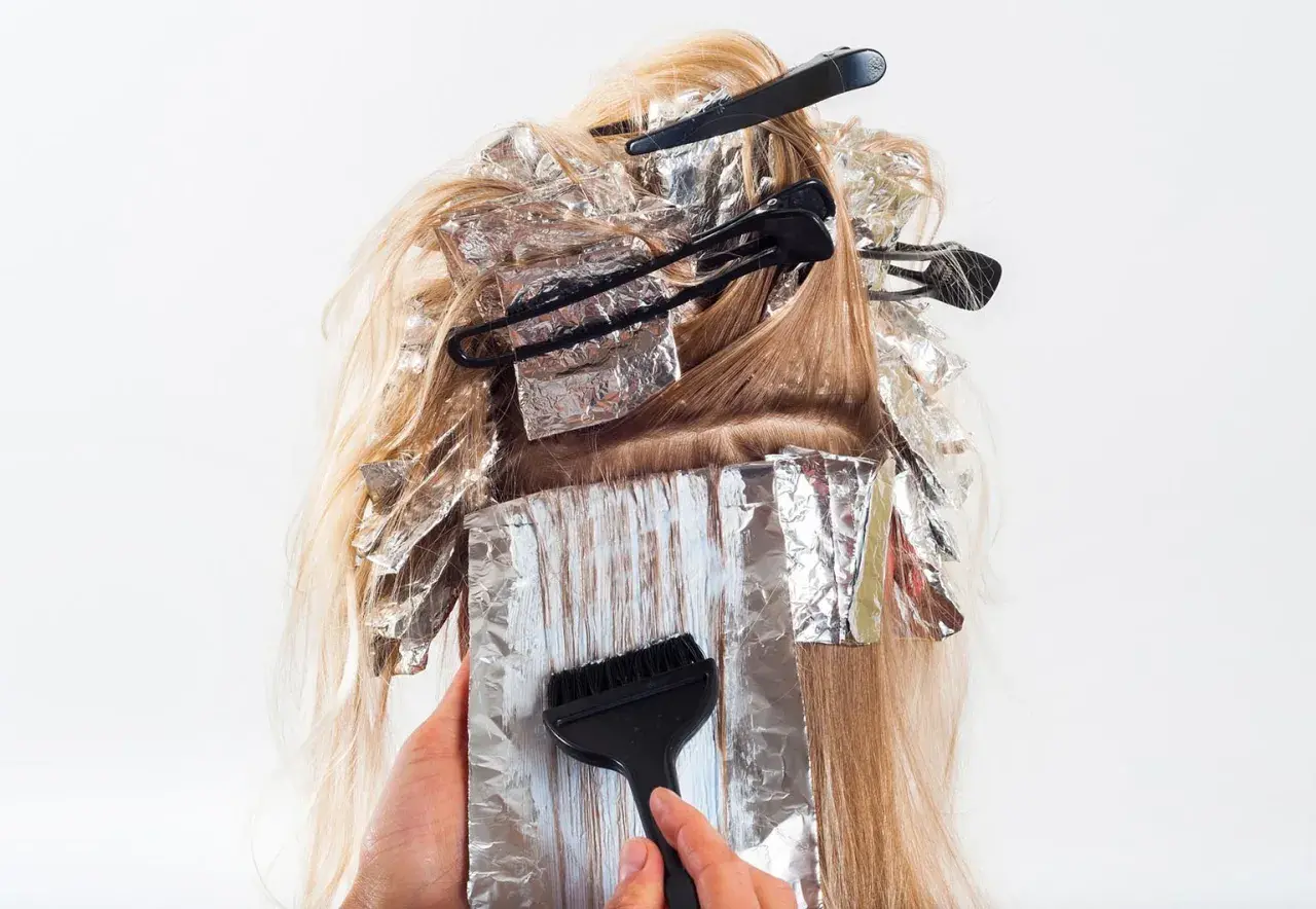 Hårstylist applicerar färg med pensel på slingor i blont hår, insvepta i folie. En blivande mamma som vill fräscha upp sitt hår.