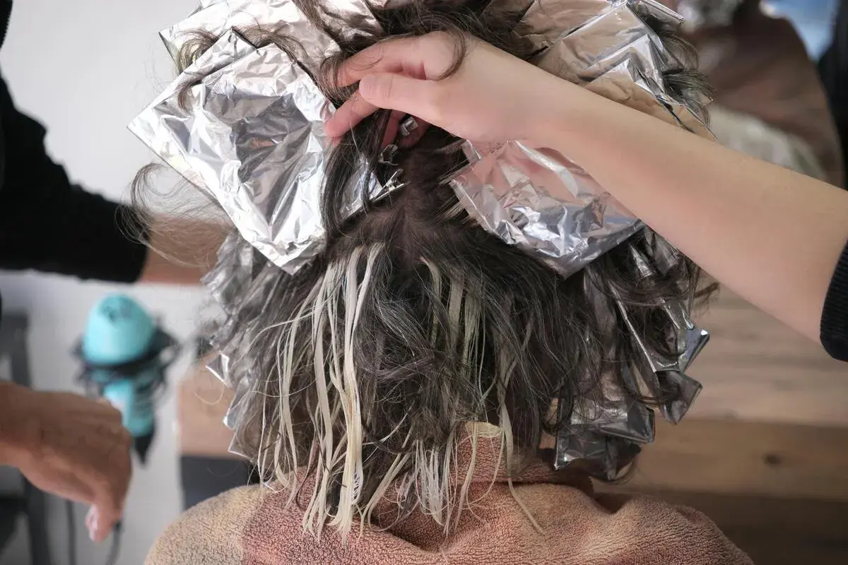 Hårstylist applicerar folie för att ta bort toning hår. Ljusare slingor syns tydligt.