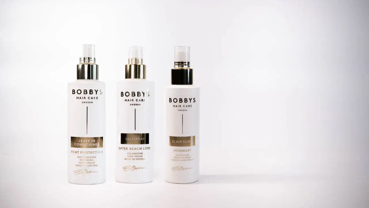 Tre flaskor Bobby's Hair Care i vitt med gulddetaljer. En leave-in conditioner för värmeskydd, en saltspray för beach look och en scalp elixir med rosmarindoft.
