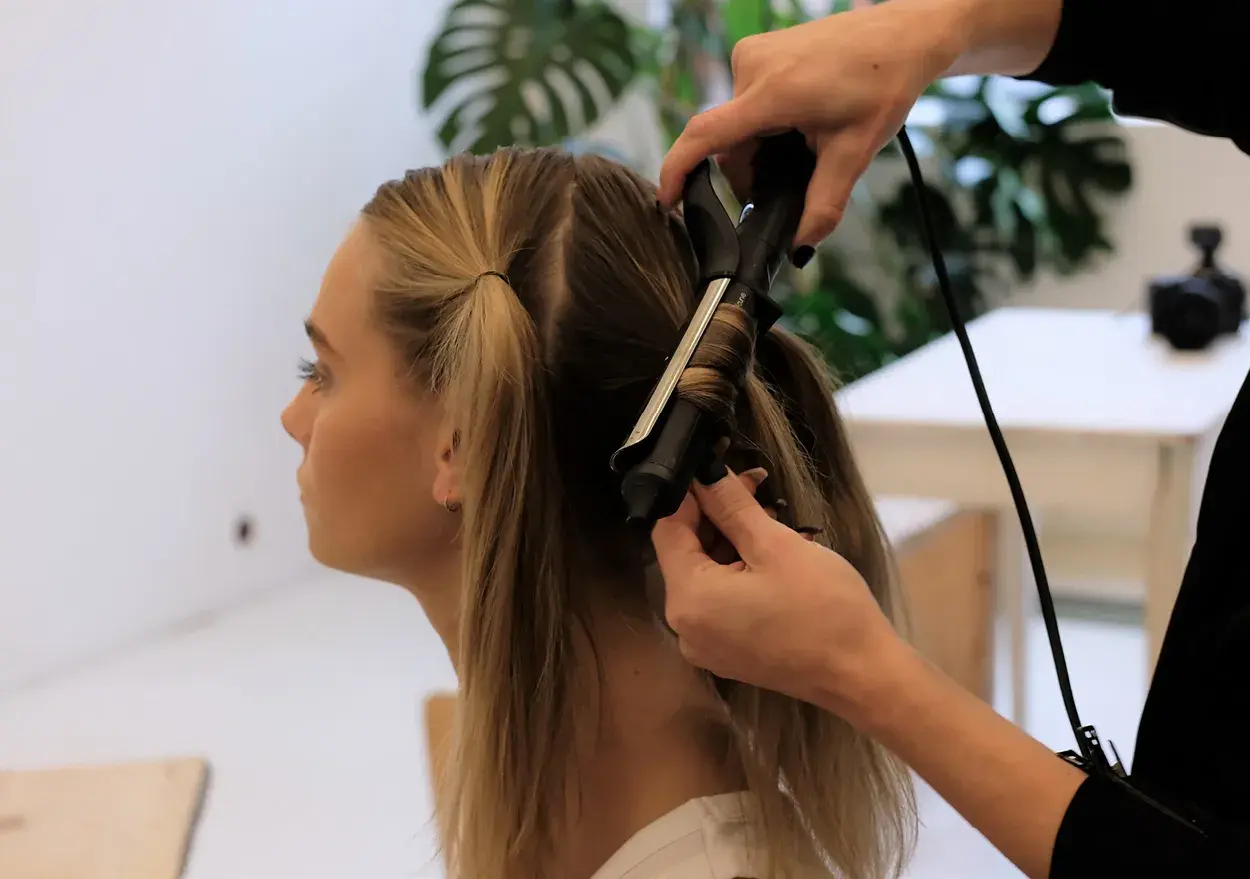 En frisör lockar en blond kvinnas hår med en locktång. En fin virvel i håret skapas.