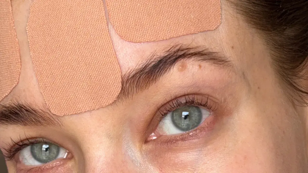Närbild på ögon och panna med hudfärgad face taping. Ögonen är gröna och har långa fransar.