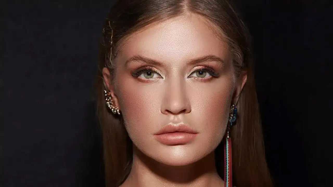 En ung kvinna med en "clean girl"-look, med subtil makeup och glänsande läppar, bär eleganta örhängen.