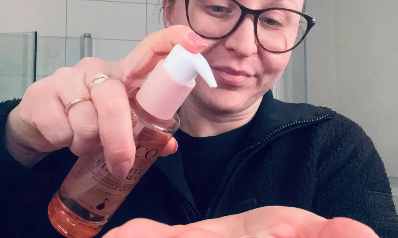 Kvinna med glasögon pumpar olja för dubbelrengöring i handen.