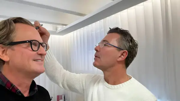 Man med glasögon får styling av sitt permanenta hår.