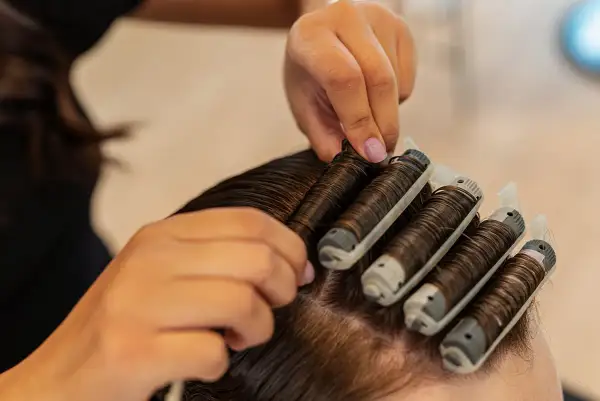 Hårstylist sätter i permanentrullar i mörkt hår. En del av processen för att se hur lång tid det tar att permanenta håret.