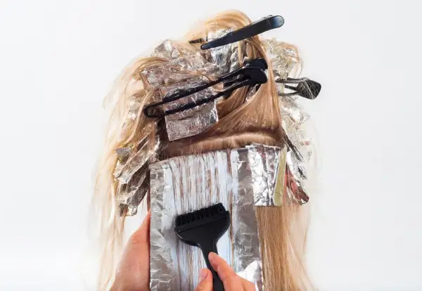 Hårstylist applicerar färg med pensel på slingor i blont hår, insvepta i folie. En blivande mamma som vill fräscha upp sitt hår.