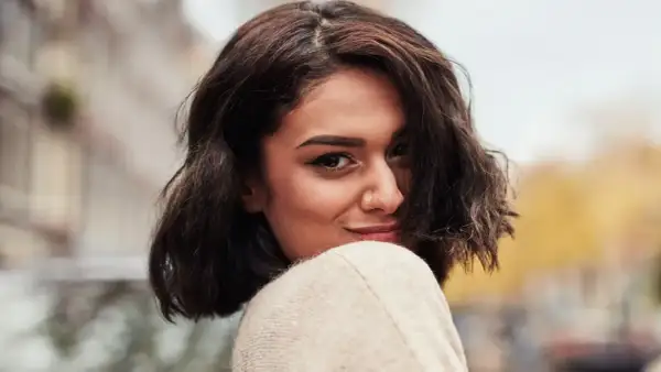 A woman with dark, wavy bob haircut and a nose ring smiles over her shoulder.