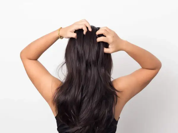 En person med mörkt hår som masserar hårbotten, en del av hårvårdsrutinen med hair oiling.