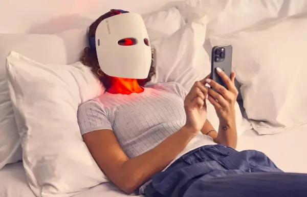 Person med led mask ansikte ligger i sängen och scrollar på mobilen.