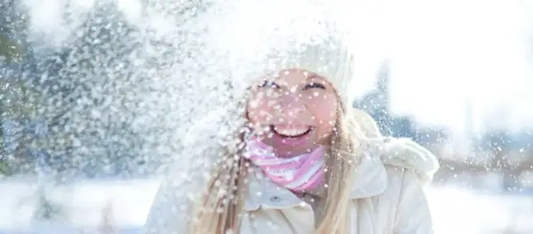Glad tjej i snöfall, med mössa och halsduk. Solskydd på vintern är viktigt, även när det snöar.